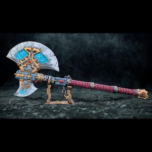 May include: A detailed fantasy axe with a silver blade, adorned with blue and gold accents and runes. The handle is wrapped in burgundy material. The axe is displayed on a small stand, showcasing its intricate design and craftsmanship.