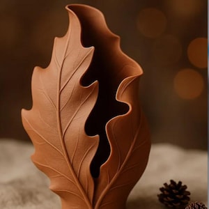 May include: A brown ceramic vase shaped like a large leaf, with detailed veining and a textured surface. The vase has a wide opening and a curved, organic form, suitable for home decor.