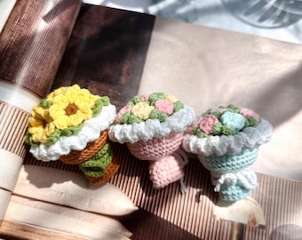 May include: Three handmade crochet flower bouquets in yellow, pink, and blue. Each bouquet features a white ruffled trim and a brown, green, or pink base. The bouquets are arranged on a magazine page.