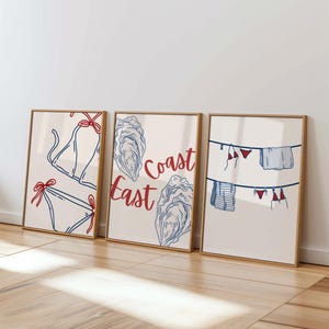 May include: Three framed prints with a nautical theme. The left print features a red and blue bikini top. The middle print features a blue and white illustration of oysters with the text "Coast East". The right print features a blue and white illustration of a clothesline with red and blue bikini tops and towels hanging on it.