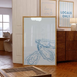 May include: A large framed print featuring a blue oyster illustration. The artwork is displayed on a wooden floor, with two other framed prints visible in the background. One print reads "Locals Only."