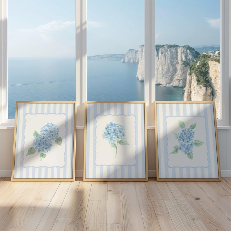 May include: Three framed watercolor prints of blue hydrangeas. Each framed print has a light blue and white striped background with a white center and a blue floral border. The frames are gold.