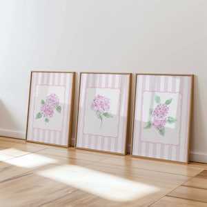 May include: Three framed floral prints featuring watercolor hydrangea blooms. Each print has a pink and white striped background with a white, scalloped-edged center. The hydrangea flowers are various shades of pink and purple with green leaves, set in a wooden frame.