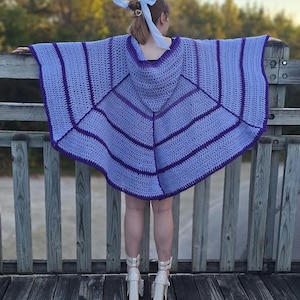 Puede incluir: Un poncho hecho a mano, tejido a ganchillo en tonos lavanda y morado. El poncho presenta una capucha y un diseño geométrico con rayas horizontales. Los bordes están ribeteados en un morado más oscuro, y la prenda se lleva sobre una parte superior oscura. La persona lleva tacones blancos.