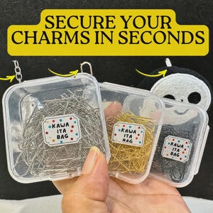 Puede incluir: Tres recipientes cuadrados de plástico transparente llenos de imperdibles de metal en plata, oro y negro. Cada recipiente tiene una etiqueta blanca con puntos de colores y el texto KAWA ITA BAG. El texto SECURE YOUR CHARMS IN SECONDS es visible.