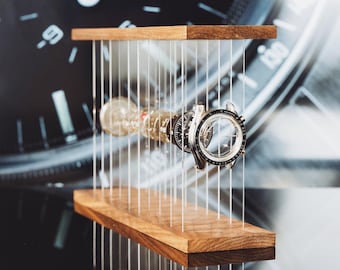 May include: A disassembled wristwatch with its components suspended horizontally between two parallel wooden planks by thin vertical wires. The watch parts, including the case, dial, and movement, are aligned in a sequence, showcasing the internal structure.