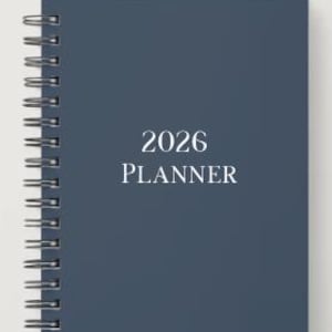 May include: A navy blue 2026 planner with a spiral binding. The text "2026 PLANNER" is centered on the cover in a white, sans-serif font. The planner is closed and appears to be new.