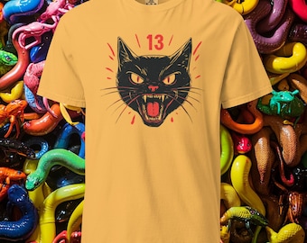 Op de afbeelding: Een geel T-shirt met een zwarte kat-print en het getal "13" erop gedrukt. De kat heeft rode ogen en gromt met zijn bek open.