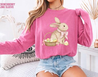 May include: A long-sleeved, pink sweatshirt with a watercolor illustration of a bunny wearing a pink bow and a basket of Easter eggs. The text "CRUNCHBERRY LONG SLEEVE" is at the top left.
