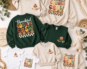 May include: A collection of beige and dark green sweatshirts and white bodysuits featuring the text Thankful Cousin Crew in retro typography, accompanied by illustrations of turkeys wearing hats and sunglasses, with some items personalized with names.