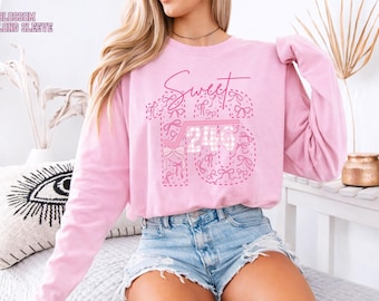 May include: A light pink long-sleeve sweatshirt with the words "Sweet 16" in a cursive font and a bow design. The number 16 is decorated with bows and the number 240 is in the center. The text "Blossom Long Sleeve" is in the upper left corner.