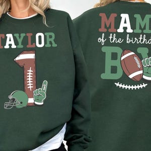 A green sweatshirt with a graphic design featuring a football, a helmet, and the text "MAMA of the birthday BOY" printed on the back.