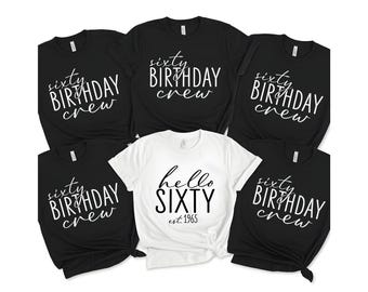 May include: A collection of black and white t-shirts. The black shirts read "sixty BIRTHDAY crew" in white script. One white shirt says "hello SIXTY est. 1965" in black script. The shirts are likely for a 60th birthday celebration.