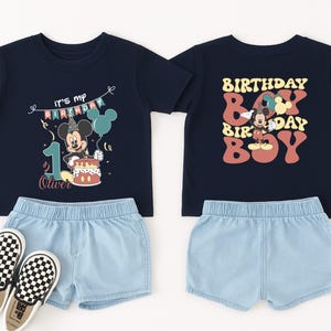 a pair of children's clothing items, including a black t-shirt with a Mickey Mouse design and a pair of shorts, along with a pair of black and white checkered shoes.