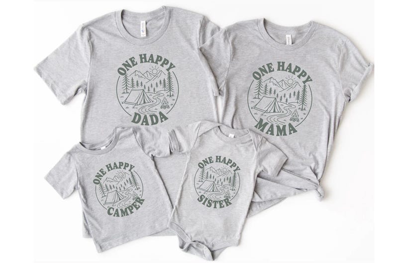 a collection of gray t-shirts with a graphic design featuring a camping scene and the text "One Happy Dada" and "One Happy Mama" printed on them.