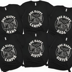 A collection of black t-shirts with white text and graphics, including camping-related designs and phrases such as "One Happy Camper", "One Happy Sister", and "One Happy Mama".