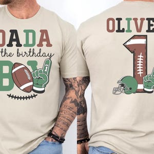 a man wearing a t-shirt with a design that says "DADA of the birthday BOY" and includes a football and a helmet.