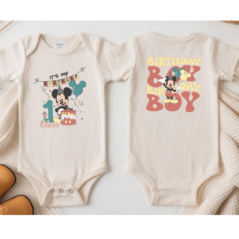 two white baby onesies with a Mickey Mouse design and text related to a birthday celebration.