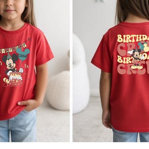 A young girl wearing a red t-shirt with a Mickey Mouse design and text on the back.