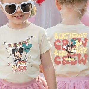 A young girl wearing a white t-shirt with a Mickey Mouse design and sunglasses, smiling at the camera.
