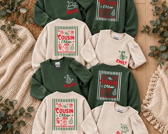 May include: A collection of dark green and beige crewneck sweatshirts featuring Christmas-themed graphics. The designs include the text "COUSIN CREW 2026" and "MAKING MEMORIES TOGETHER" alongside illustrations of trees, candy canes, and gifts.
