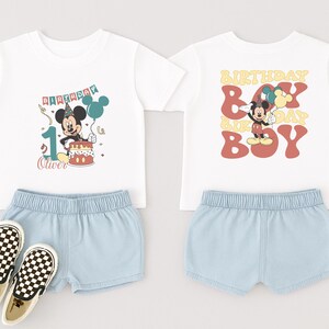 a pair of white t-shirts with Mickey Mouse designs, a pair of blue shorts, and a pair of checkered shoes.