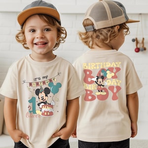 A young boy wearing a Mickey Mouse-themed t-shirt and a baseball cap, smiling and posing for the camera.