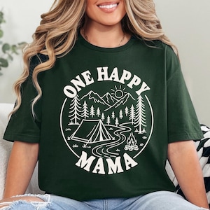 A woman wearing a green t-shirt with a graphic design that says "One Happy Mama" and features a camping scene with mountains, pine trees, and a campfire.