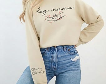 May include: A beige sweatshirt with the words "dog mama" in black script and a line drawing of hands holding a paw. The left sleeve has the names "Luna & Bailey" in script with paw prints.