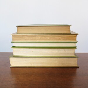 K&ouml;nnte beinhalten: Ein Stapel von f&uuml;nf B&uuml;chern mit gr&uuml;nen und braunen Einb&auml;nden. Die B&uuml;cher sind pyramidenf&ouml;rmig auf einer Holzoberfl&auml;che angeordnet.