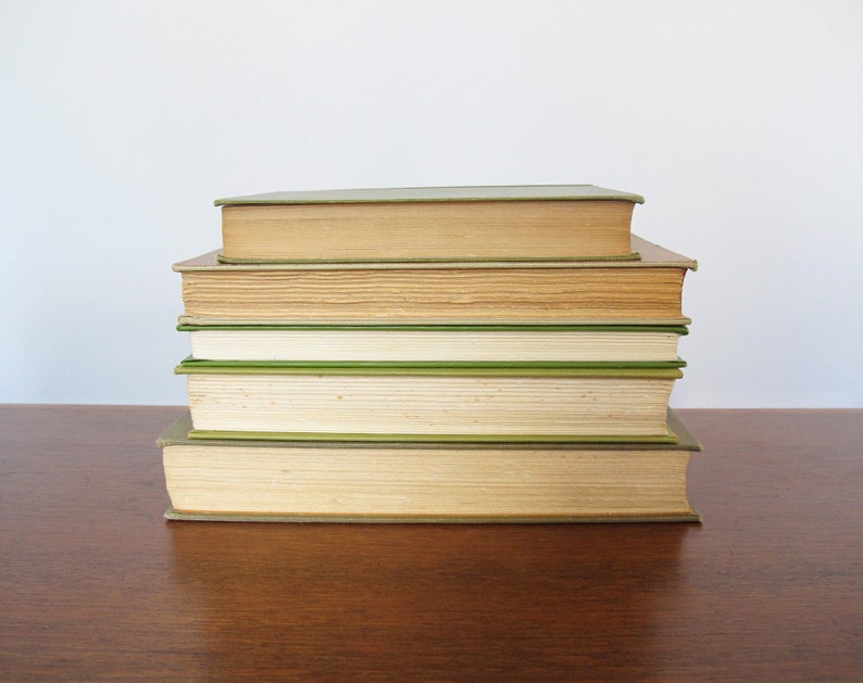 K&ouml;nnte beinhalten: Ein Stapel von f&uuml;nf B&uuml;chern mit gr&uuml;nen und braunen Einb&auml;nden. Die B&uuml;cher sind pyramidenf&ouml;rmig auf einer Holzoberfl&auml;che angeordnet.