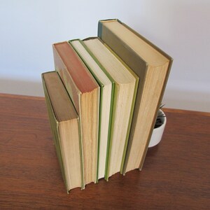 K&ouml;nnte beinhalten: Ein Stapel von f&uuml;nf Vintage-Hardcover-B&uuml;chern mit gr&uuml;nen und braunen R&uuml;cken. Die B&uuml;cher sind in einem vertikalen Stapel angeordnet, wobei das h&ouml;chste Buch unten und das kleinste Buch oben liegt.
