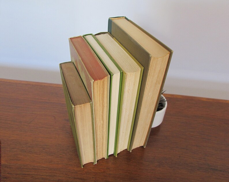 K&ouml;nnte beinhalten: Ein Stapel von f&uuml;nf Vintage-Hardcover-B&uuml;chern mit gr&uuml;nen und braunen R&uuml;cken. Die B&uuml;cher sind in einem vertikalen Stapel angeordnet, wobei das h&ouml;chste Buch unten und das kleinste Buch oben liegt.