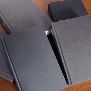 May include: A stack of five black hardback books with smooth, textured covers.
