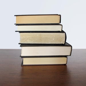May include: A stack of five books with black covers and cream coloured pages. The books are arranged in a neat pile on a wooden surface.
