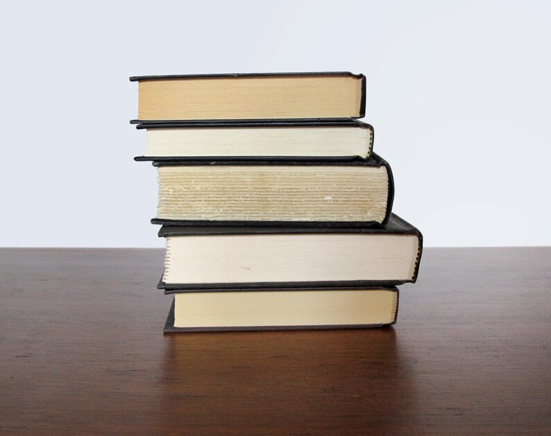 May include: A stack of five books with black covers and cream coloured pages. The books are arranged in a neat pile on a wooden surface.