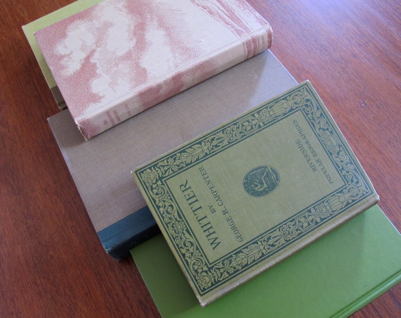 K&ouml;nnte beinhalten: Ein Stapel von vier B&uuml;chern mit gr&uuml;nen, braunen und cremefarbenen Einb&auml;nden. Das oberste Buch hat ein goldfarbenes Design und den Text "WHITTIER" und "GEORGE R. CARPENTER" auf dem vorderen Einband. Der Text "POULAR RIVERSIDE" und "LIBRARY" ist ebenfalls auf dem Einband zu sehen.