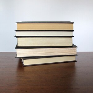 May include: A stack of six books with black covers and cream coloured pages. The books are stacked on a wooden surface.