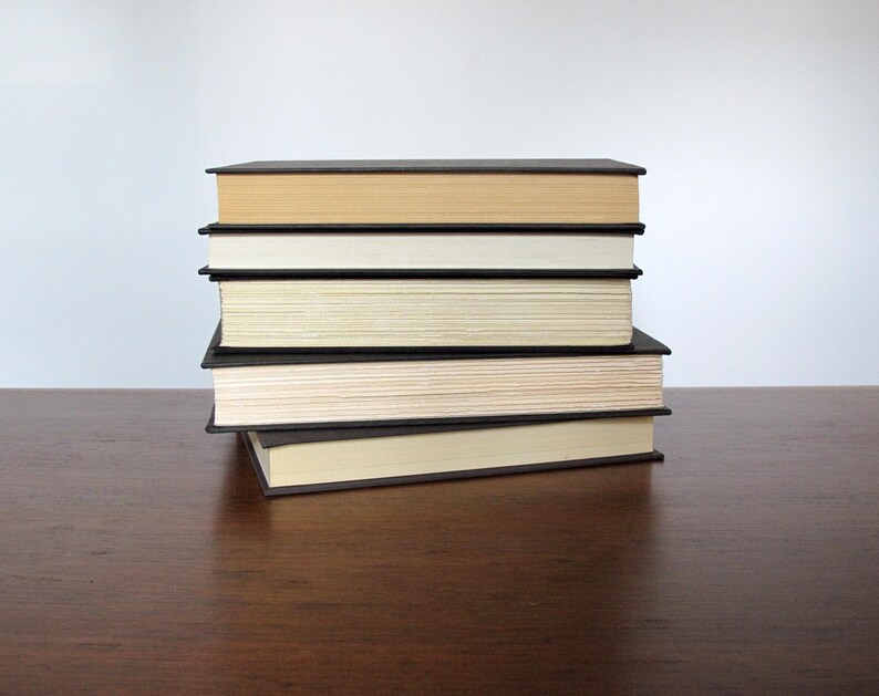May include: A stack of six books with black covers and cream coloured pages. The books are stacked on a wooden surface.