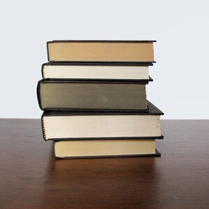 May include: A stack of five books with black covers and different coloured spines. The books are arranged in a pyramid shape, with the largest book at the bottom and the smallest book at the top. The books are sitting on a wooden surface.