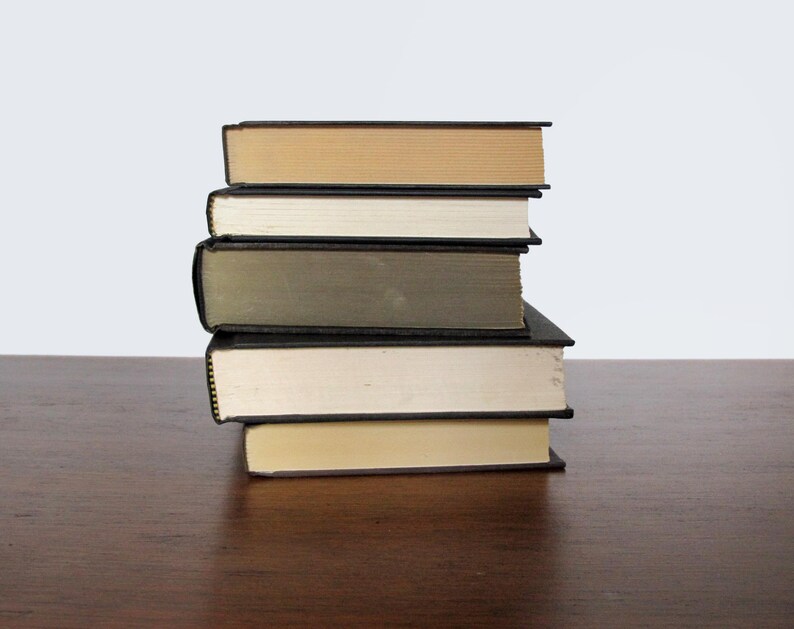 May include: A stack of five books with black covers and different coloured spines. The books are arranged in a pyramid shape, with the largest book at the bottom and the smallest book at the top. The books are sitting on a wooden surface.