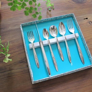 May include: A set of six silver-plated utensils in a blue box with a white floral pattern. The set includes two forks, two spoons, and two knives.