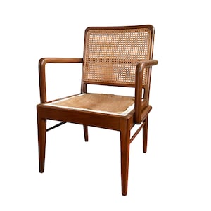 May include: A wooden armchair with a woven cane back and seat. The chair has armrests and a warm brown finish. The seat cushion appears to be made of a natural fiber material. The chair is set against a white background.