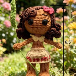 May include: A handmade crochet doll, approximately 6.5 inches tall, with brown skin, dark brown curly hair, and a red bow. The doll wears a beige skirt with red accents and holds a green leaf. The doll has large black eyes.