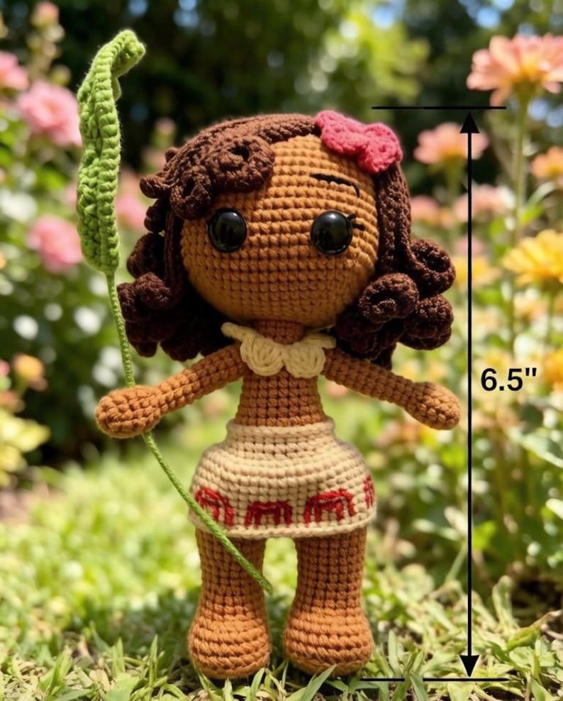 May include: A handmade crochet doll, approximately 6.5 inches tall, with brown skin, dark brown curly hair, and a red bow. The doll wears a beige skirt with red accents and holds a green leaf. The doll has large black eyes.