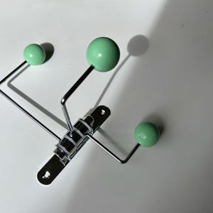 May include: A chrome coat rack with three mint green ball-shaped hooks.