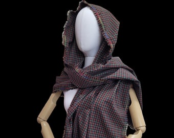 May include: A hooded scarf with a plaid pattern in shades of black, red, and green. The scarf has a frayed edge and is made of a soft, woven fabric.