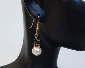 May include: Gold dangle earrings with a single white pearl and purple beads.