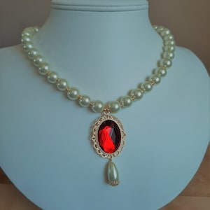 May include: A white pearl necklace with a gold pendant featuring a large red gemstone and a smaller pearl drop.