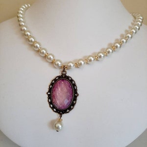 May include: A pearl necklace with a pink cameo pendant and a single pearl drop. The cameo is set in a gold-toned filigree frame.